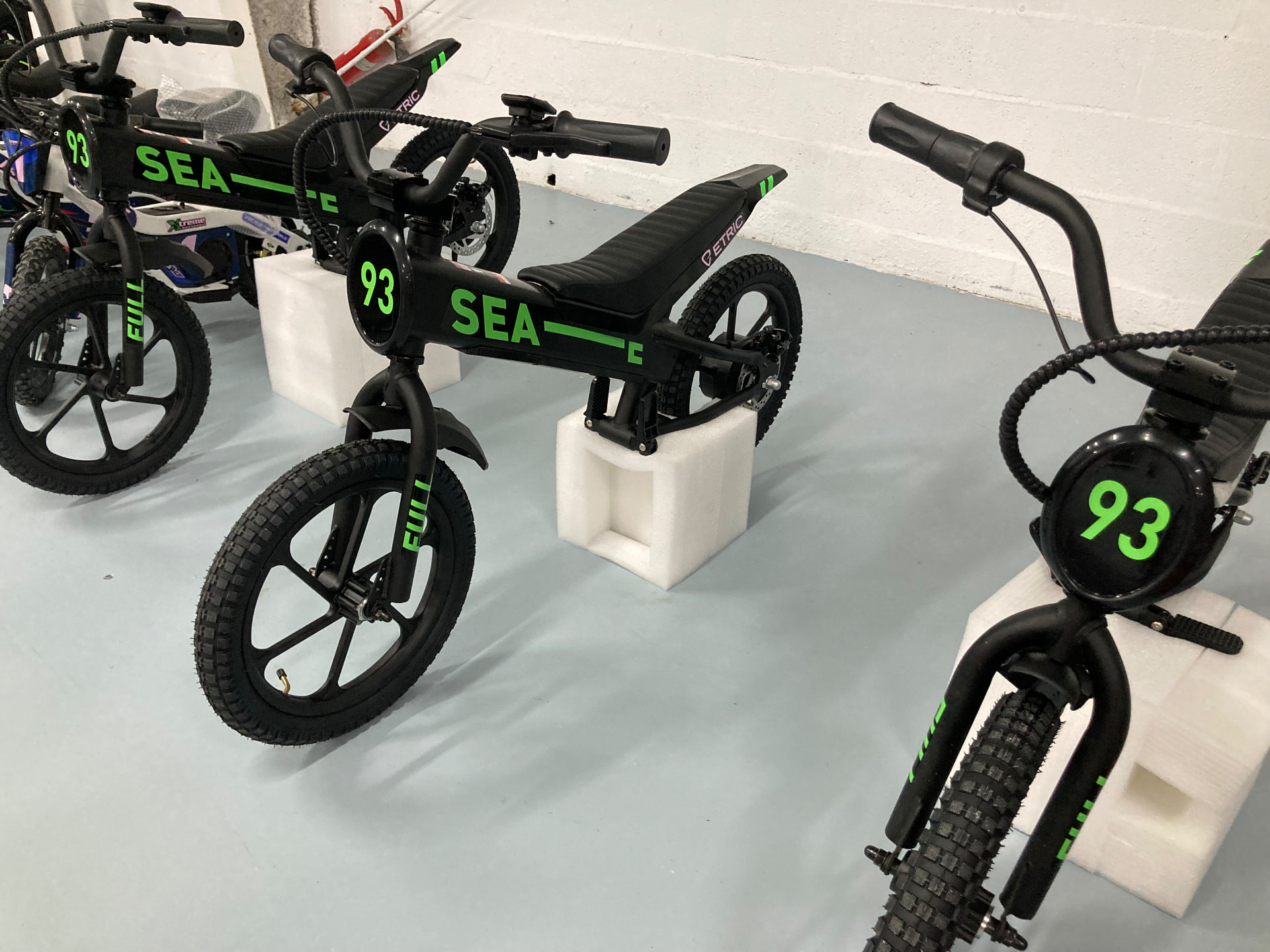 Bicicletas eléctricas infantiles tipo pit bike en negro mate con gráficos verde flúor y el dorsal 93 apoyadas sobre espumas de embalaje