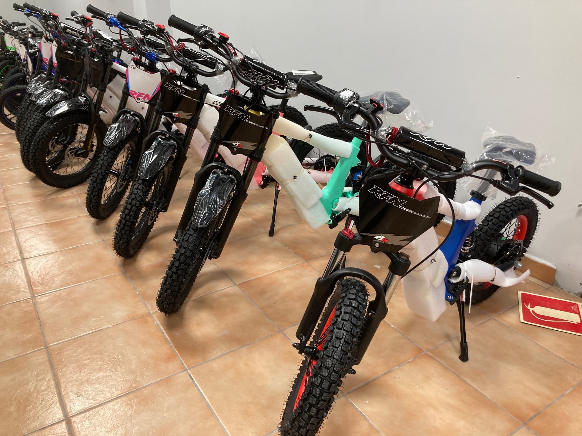 Bicicletas eléctricas juveniles RFN EVO Racing en azul, blanco y verde menta expuestas en fila en la tienda