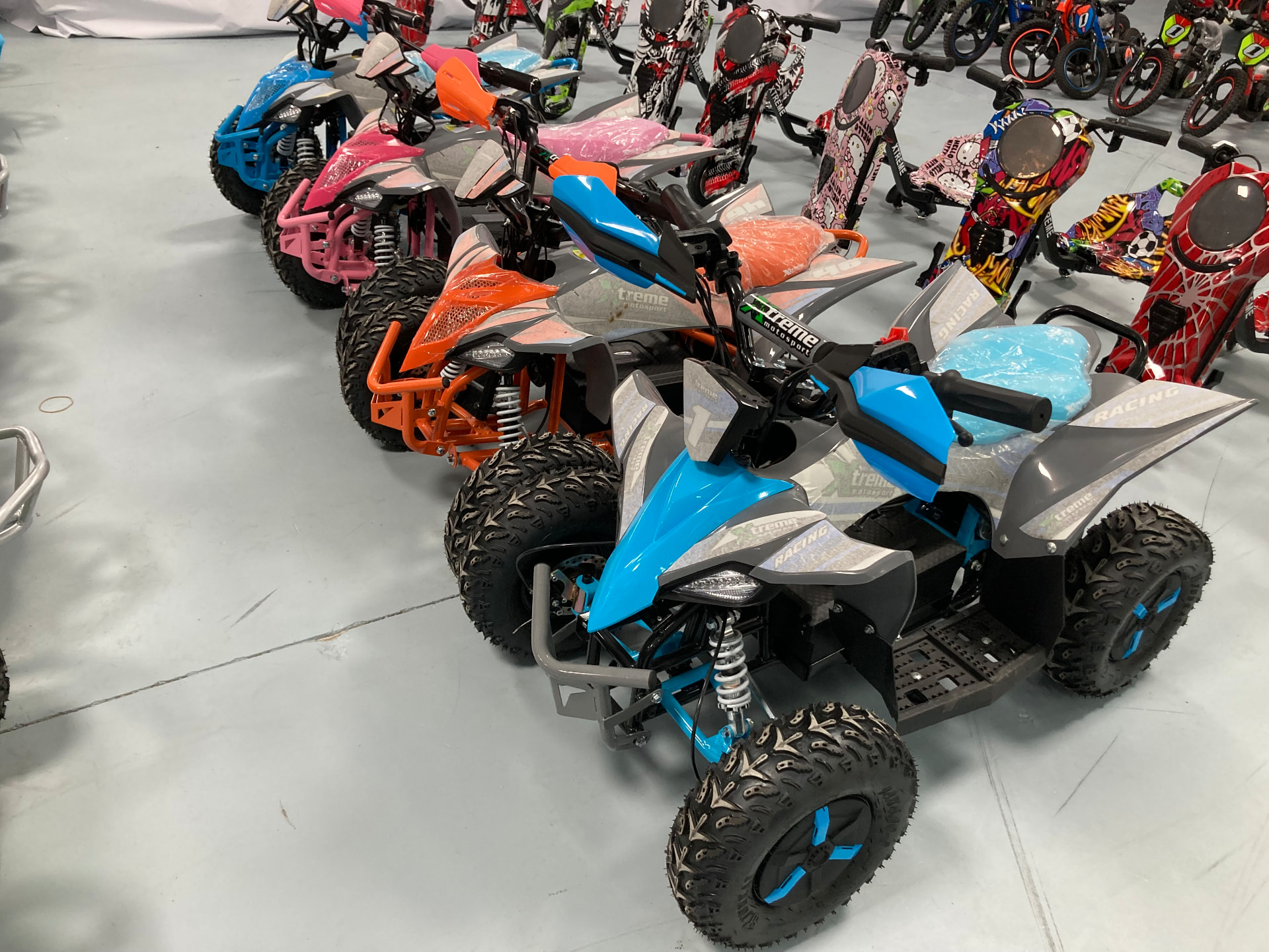 Miniquads eléctricos Xtreme en azul, naranja y rosa con el dorsal 1 en la exposición