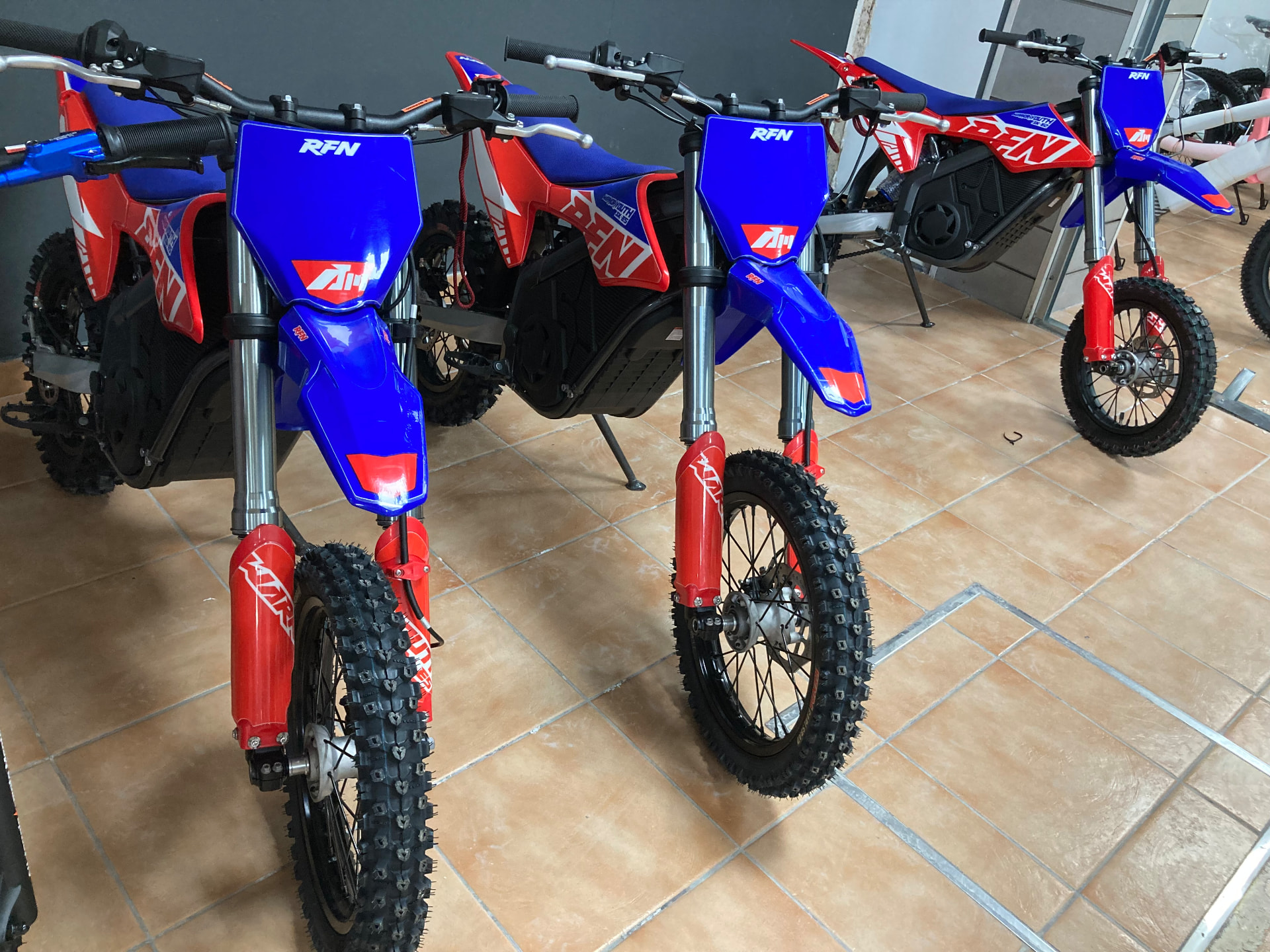 Motos de cross eléctricas RFN Warrior Youth en azul, rojo y blanco en la exposición