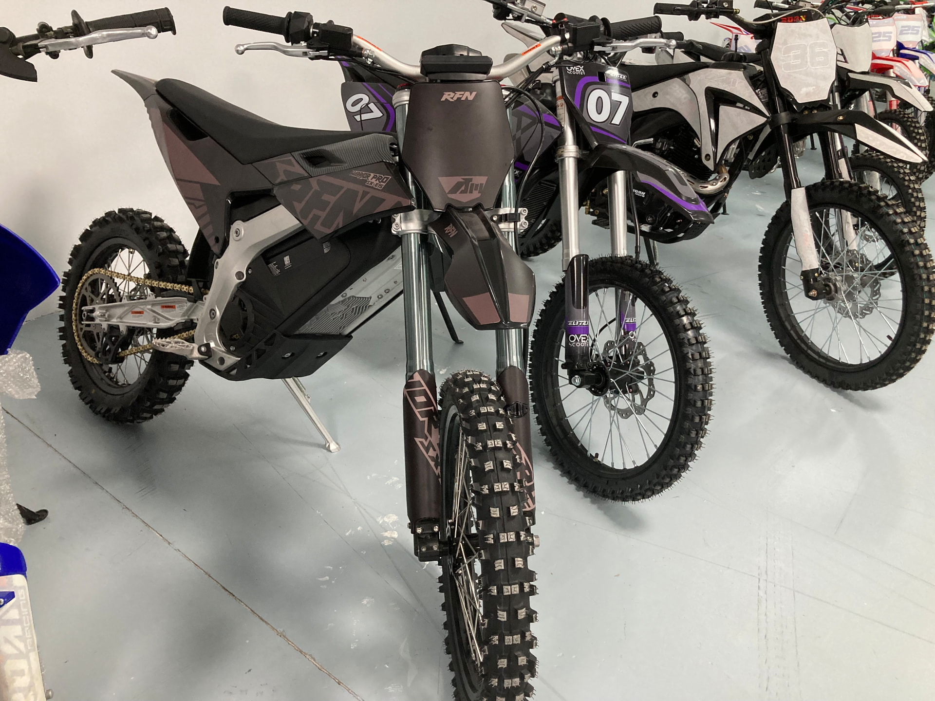 Moto de cross eléctrica RFN Warrior Pro en negro mate junto a otras motos en la tienda