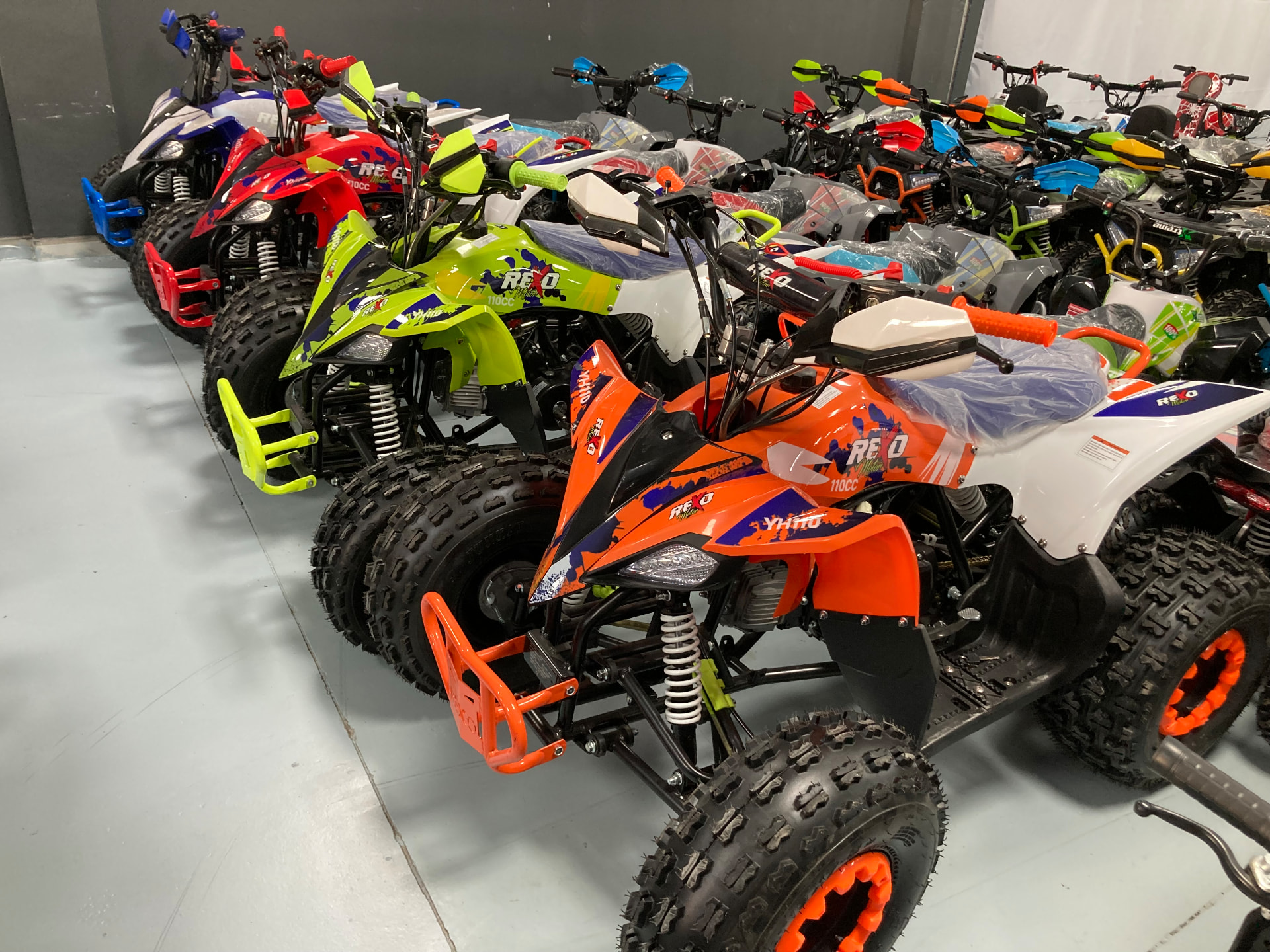 Fila de quads REXO 110cc en naranja, verde, rojo y blanco en la exposición